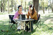 © NAMPIX - Two young Asian women wearing headphones, sitting at a portable table in a park and working or studying together