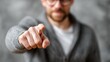 © phy - A man in a gray sweater pointing at the camera with his index finger, wearing glasses and a beard, against a blurred background.