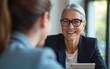 © Matthew - Smiling aged businesswoman in glasses looking at colleague at team meeting, happy attentive female team leader listening to new project idea, coach mentor teacher excited by interesting discussion