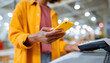 © Mary - Close-up of shopper using a yellow smartphone for wireless payment at a card terminal, highlighting modern retail and cashless technology.