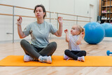 Mother and daughter child sit on a mat and practice yoga exercises in the gym