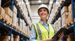 © Vasiliy - Smiling female warehouse worker with a clipboard checking inventory. Professional logistics manager in a hard hat standing in a large distribution center