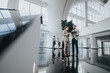 © qunica.com - Two colleagues in smart suits talk and review a tablet in a bright, contemporary office lobby as others mingle in the background.