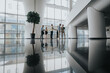 © qunica.com - Bright, spacious office lobby with large windows and a reflective floor. Colleagues gather, review documents, and greet each other, creating a collaborative atmosphere in a contemporary work setting.
