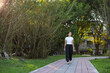 © leungchopan - Woman walking in green city park on sunny day