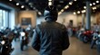 © Alex Pios - Man in leather jacket, helmet chooses new motorcycle in dealership. Biker client looks at motorbikes for sale inside modern showroom. Customer buying transport, picking vehicle for travel, adventure