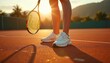 © Vadym - Woman tennis player stands on clay court with racket at sunrise. Close-up of female legs in white sneakers ready for sport match workout. Girl enjoys active lifestyle, fitness training outdoors on