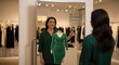 © Hungarian - Woman uses interactive mirror displaying a virtual green dress overlay in a modern apparel store