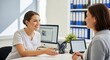 © photoplotnikov - Two female colleagues discuss projects in modern office setting
