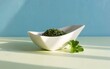 © Fahad - Dried chopped parsley herbs in white bowl, fresh green leaf garnish, minimalist blue background, organic food seasoning, sunlight shadow texture, for cooking, kitchen, spice.