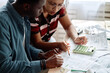 © Seventyfour - Young Black man and young Black woman analyzing invoices and bills together at desk, using calculator and pen, collaborating on financial paperwork and calculations