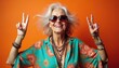 © Vadym - Senior woman with grey hair wears floral shirt sunglasses and jewelry. She smiles making peace signs with hands. Vibrant colors suggest energy and happiness.