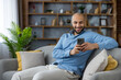 © Liubomir - Smiling man relaxing on sofa using smartphone for communication