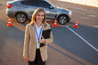 © Andrii  - Smiling driving instructor holding clipboard near learner car on test site