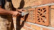 © DigitalSpace - Medium shot of a worker fitting traditional clay ventilation bricks into a brick wall enhancing natural airflow with rustic textured materials.