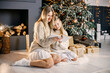 © prostooleh - Young mother and little girl sitting christmas tree at home and reading a book