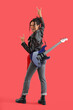 © Pixel-Shot - Happy young African-American woman in leather jacket with electric guitar showing 'devil horns' gesture on red background