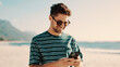 © FlexOn/peopleimages.com - Man, scroll and smile with phone at beach for social media joke, funny online meme and summer holiday. Happy person, typing and vacation with tech by ocean for mobile app, internet humor and space.