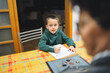 © Fotografia Juan Reig - Young boy concentrating on his schoolwork, sitting at a kitchen table while his grandmother provides quiet guidance and support with his education and learning