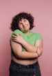 © bodnarphoto - Young person in a green shirt stands against a pink background with a joyful expression, showcasing confidence and self-acceptance