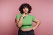 © bodnarphoto - Thoughtful teenager with curly hair poses against pink background in casual green shirt and black pants