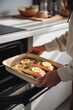 © Katerina Bond - A woman places a baking tray of fresh salmon with lemon and herbs into a modern oven in a bright kitchen, captured in natural morning light.