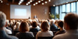 © perfectlab - Audience attending a conference or seminar in a modern meeting room with a speaker presenting on stage and a large projection screen