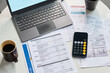 © pressmaster - Closeup of financial documents, calculator, laptop and coffee cup on table showing tax forms and utility bills, illustrating process of calculating and paying taxes at home or office
