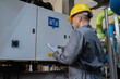 © reewungjunerr - Professional technician inspecting electrical control panel in a factory plant. Male engineer recording operational data on clipboard during safety maintenance of industrial machinery system.