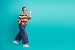 © deagreez - Mature woman waves happily against teal background in striped sweater and jeans