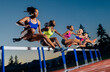 © Connect Images - Group of athletes jumping over hurdles on a running track at sunset in vibrant sportswear. WA, USA