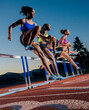 © Connect Images - Three athletes in mid-air leap over hurdles on an outdoor track at dusk. WA, USA