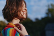 © SHOTPRIME STUDIO - Woman smiling in a colorful striped sweater, short hair, young adult portrait outdoors in nature, casual outfit and relaxed pose, hand near collar, joyful lifestyle and travel vibe.