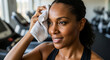 © SYATRI RAWU - Close-up of a determined African American woman wiping sweat from her forehead with a white towel after an intense workout at the fitness center
