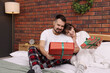 © New Africa - Happy couple in pajamas with gift boxes spending time together on bed in room decorated for Christmas