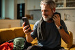© Marko Geber - Mature man smiling with smartphone after workout at home