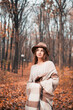 © Тамара Печеная - Woman in cozy sweater and hat enjoying a stroll in a forest filled with autumn leaves
