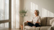 © Kamlesh - Senior asian woman meditating peacefully on a cozy sofa in a sunlit living room at home, finding inner peace