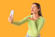 © Pixel-Shot - Beautiful young woman with modern mobile phone blowing kiss while taking selfie on yellow background
