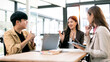 © NAMPIX - Three cheerful young Asian business professionals engaging in an animated discussion and collaboration meeting in a bright, modern office space.