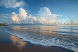 Sandy shoreline with gentle foamy waves, reflective wet sand and towering white cumulus clouds under a golden blue sky, evoking peaceful tranquility