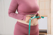 © Pixel-Shot - Sporty woman with excess weight measuring her waist at home