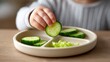 © CreativeArt - Child's hand holding a fresh cucumber slice, encouraging healthy eating and independent feeding development