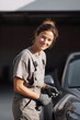 © Olena - Smiling female mechanic in overalls, holding tools near a vehicle. Empowerment, skilled trades, automotive repair, and women in STEM themes.