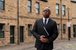 © Iryna - Business professional in formal attire stands thoughtfully outside historic stone buildings in a city setting
