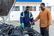 © Roger - African mechanic in blue overalls explains an engine issue to a customer in his workshop