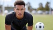 © pkproject - Close up portrait of a focused young male athlete with athletic build and curly hair wearing a black sports shirt on a grassy field with a soccer ball in the background