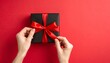 © Argiduna - Fotografía en primera persona en vista superior, de unas manos atando un lazo de cinta roja en una caja de regalo negra, sobre un fondo rojo.