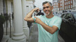 © Krakenimages.com - Man flexes bicep and points to arm on a city street framed by townhouse columns and parked car; confidence vitality.