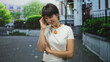 © Krakenimages.com - Woman touching forehead with hand and crossed arms on street wearing white tshirt and orange pendant; shyness introspection.